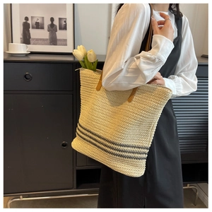 Detail of woven straw tote bag featuring grey stripes and premium brown leather handle