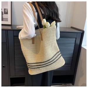 Detailed side view of large straw tote bag with black stripes and brown leather straps