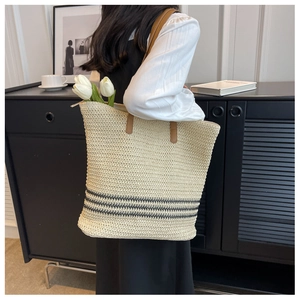 Detail of woven straw tote bag featuring black stripes and brown leather handles