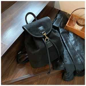 Detail of black suede backpack with gold hardware hooks on a rustic wooden staircase