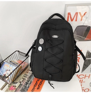 Détail du sac à dos en nylon noir avec cordons élastiques, badges et style collège