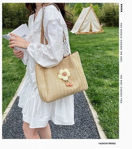 Detail of straw woven tote bag featuring floral decor and brown leather chain strap