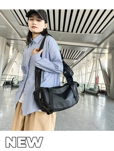 Detail of a black cylindrical travel bag with wide strap and mini pouch in a station