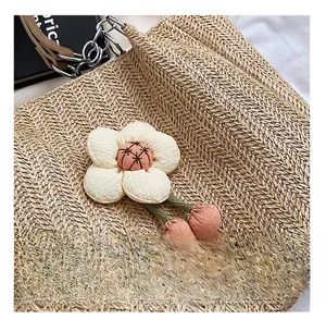 Detail of woven straw tote bag featuring decorative white flowers and pink fabric pendants