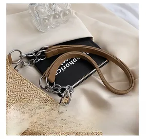 Detail of beige straw tote bag featuring brown leather straps and silver metal hardware rings