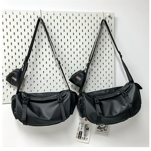 Close-up of dual black nylon messenger bags with shiny finish and mini pouch on pegboard