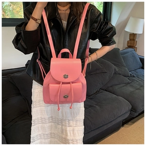 Gros plan du mini sac à dos en cuir rose avec fermoirs rotatifs argentés sur canapé