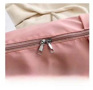 Detail of pink oxford fabric bag featuring a gold-toned dual metal zipper and embroidery