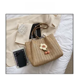 Detail of light brown straw tote bag with white flower charms and dark leather handles