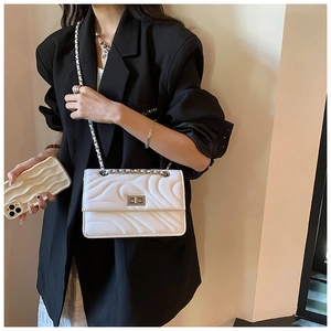 Détail de la texture en cuir blanc matelassé et chaîne argentée sur un petit sac bandoulière