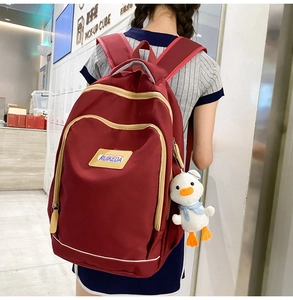 Detail view of burgundy waterproof nylon backpack with white duck charm and tan trim zippers