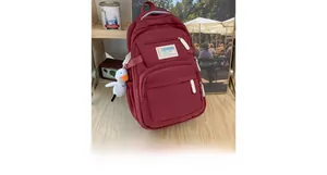 Detail of red travel backpack with side pockets and a small white duck charm on a desk