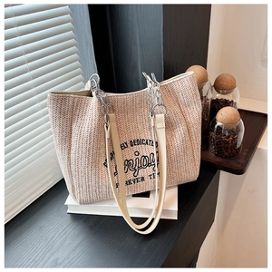 Detail of woven straw tote bag texture with black printed text and metal chain straps
