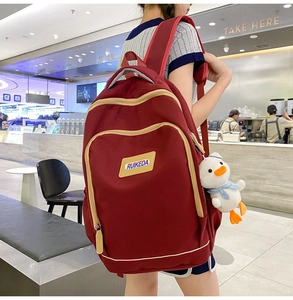 Detail showing deep red casual backpack with plush duck charm and brand logo label