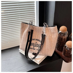 Detailed close-up of a woven straw tote bag with black embroidery and chain straps