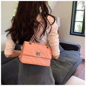 Détail du sac matelassé corail avec fermoir argenté porté par un mannequin en intérieur