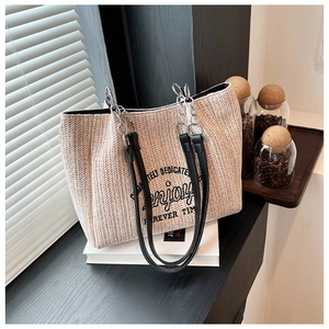 Detail of woven straw tote bag with black Enjoy text and leather chain shoulder straps