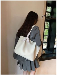 Detail of a large cream tote bag with textured leather and a pink checkered scarf on handle