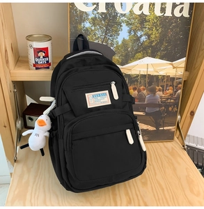 Detail of black canvas backpack with white zippers, multi-pockets and duck charm