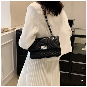 Détail d'un sac à bandoulière en cuir noir matelassé avec chaîne argentée et fermoir pivotant