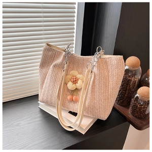 Detail of woven straw tote bag with floral charms and leather chain shoulder strap