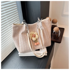 Detail of hand-woven straw tote bag with decorative flower and metal chain strap