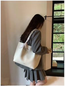 Detail of minimalist cream tote bag with lychee texture and plaid ribbon on the handle