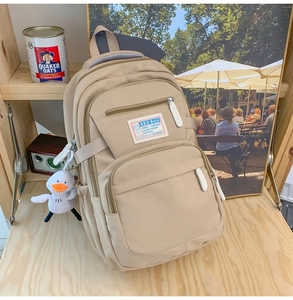 Detail view of khaki multi-pocket nylon backpack with plush duck charm on a wooden table