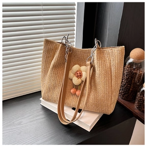 Detail of woven straw tote with fabric flower decor, leather strap, and orange pom poms