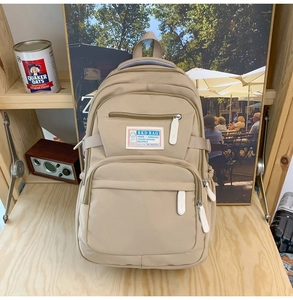 Detail view of beige nylon backpack featuring multiple zippers and side elastic pockets