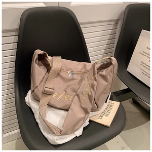 Detail of taupe oxford crossbody bag featuring wide strap and yellow cursive embroidery