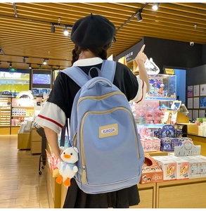 Detail of light blue nylon backpack with multiple pockets and a cute duckling pendant