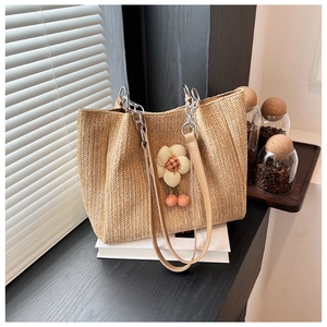 Detail of handwoven straw tote bag with floral pendant and brown leather handles