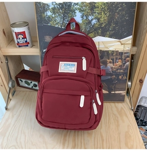 Detail of burgundy multi-pocket backpack with logo patch on a minimalist wooden shelf