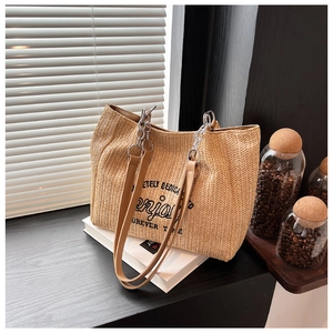 Detail of woven straw tote bag with brown leather straps and silver chain accessories