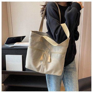 Close-up of beige canvas tote bag with dual front zipper pockets and wide shoulder straps