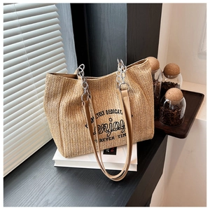 Detail of woven straw tote bag with chain strap resting on books in sunlight