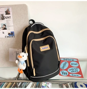 Detailed view of black canvas backpack with beige straps and a plush duck accessory