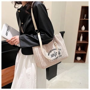 Detail shot of beige woven straw tote bag with black enjoy lettering and shoulder strap