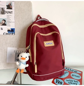 Detail view of burgundy canvas backpack featuring a plush duck pendant and multi-layer pockets