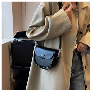 Detail shot of a black leather saddle bag with silver hardware on a beige trench coat