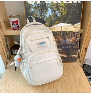 Detail view of off-white multi-pocket backpack with small duck plush charm accessory