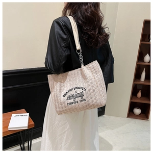 Macro detail of beige woven tote bag with black embroidery and chain leather strap