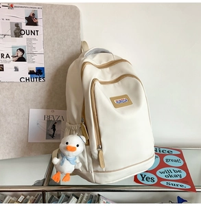 Close-up of white casual backpack with brown trim and cute duck plush charm accessory