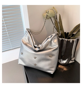 Detail of silver metallic tote bag featuring chain straps and heart metal ornament