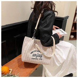 Detail of woven straw tote bag with black embroidery and premium leather shoulder strap