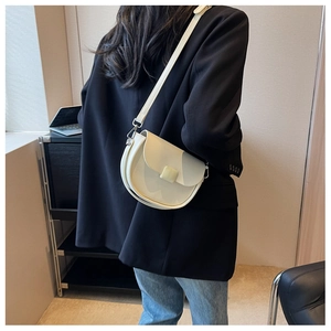 Model wearing ivory half-moon saddle bag with adjustable strap over black blazer