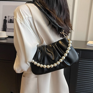 Elegant black pleated cloud bag with pearl chain strap worn by a model in soft lighting