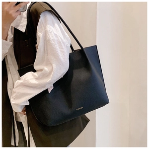 Close-up of black lychee grain leather tote bag with gold logo and slim straps