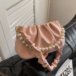 Elegant pink pleated cloud bag with pearl strap and gold hardware on black sofa